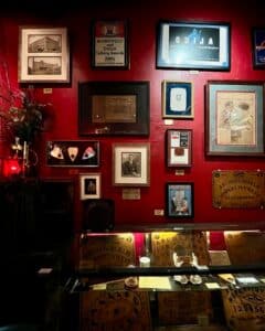 A vibrant red wall at the Salem Witch Board Museum in Salem, Massachusetts, adorned with vintage Ouija advertisements, photographs, and historical memorabilia, with glass cases of spirit boards below.