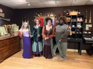 A group of four people dressed as characters from Hocus Pocus, standing inside The Witchery boutique surrounded by witch-themed decor, brooms, and mystical items.