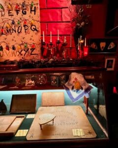 A well-lit Ouija board exhibit with vintage boards, a festive backdrop featuring candelabras and colorful string lights, at the Salem Witch Board Museum in Salem, Massachusetts.