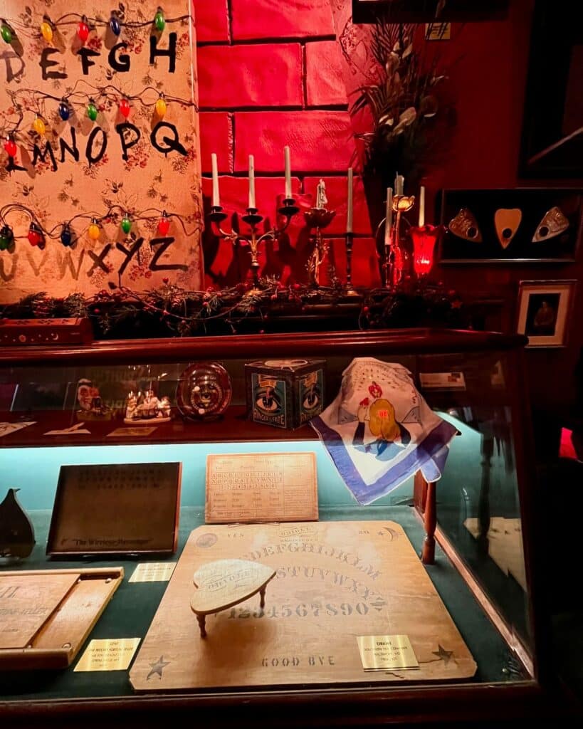 A well-lit Ouija board exhibit with vintage boards, a festive backdrop featuring candelabras and colorful string lights, at the Salem Witch Board Museum in Salem, Massachusetts.