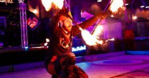 A fire performer in Salem Massachusetts kneeling on stage, skillfully spinning flaming props under vibrant festival lights at the Frozen Fire Festival.