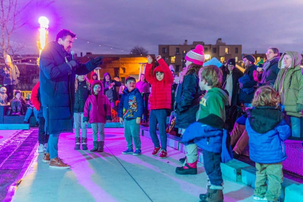 A lively group of children engaging in a fun activity led by a host during the Salem Frozen Fire Festival in Salem Massachusetts, with a colorful evening backdrop.