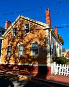 Side view of the Jonathan Whipple House in Salem, Massachusetts, featuring its warm yellow clapboard siding, white-trimmed gable roof, and red brick chimneys under a vibrant blue sky.