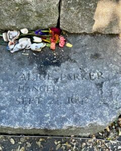 A memorial stone at the Salem Witch Trials Memorial in Salem, Massachusetts, honoring Alice Parker, engraved with her name and the date of her execution, September 22, 1692. Flowers and seashells are left on the stone as tributes.