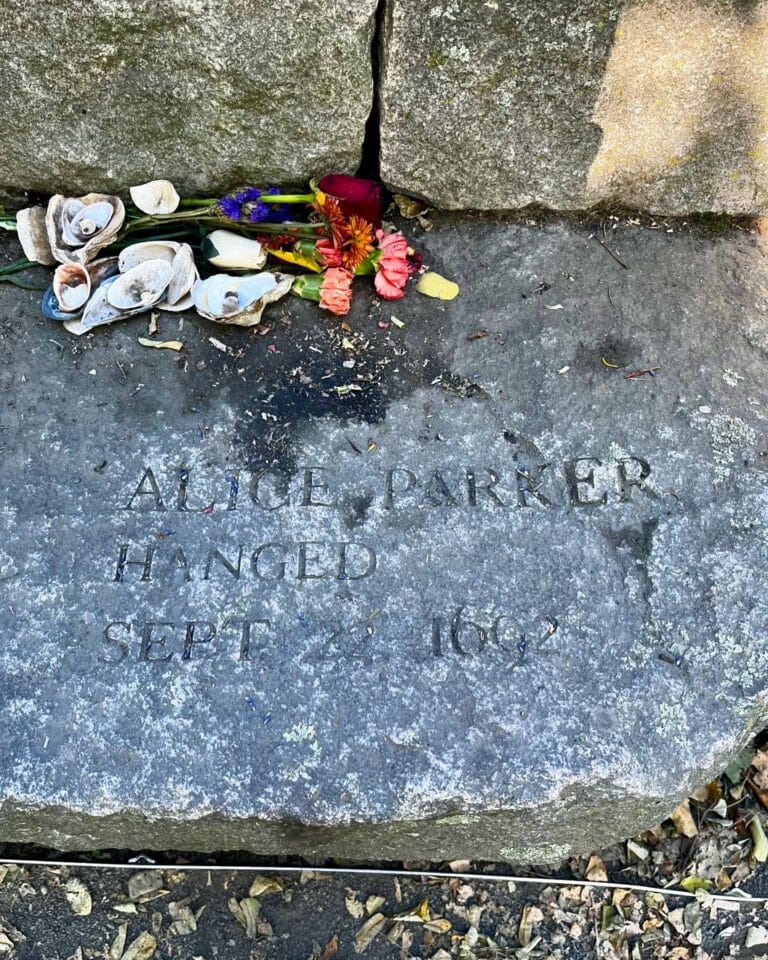A memorial stone at the Salem Witch Trials Memorial in Salem, Massachusetts, honoring Alice Parker, engraved with her name and the date of her execution, September 22, 1692. Flowers and seashells are left on the stone as tributes.