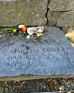 A memorial stone at the Salem Witch Trials Memorial in Salem, Massachusetts, honoring Martha Corey, engraved with her name and the date of her execution, September 22, 1692. Flowers and seashells rest on the stone as offerings.