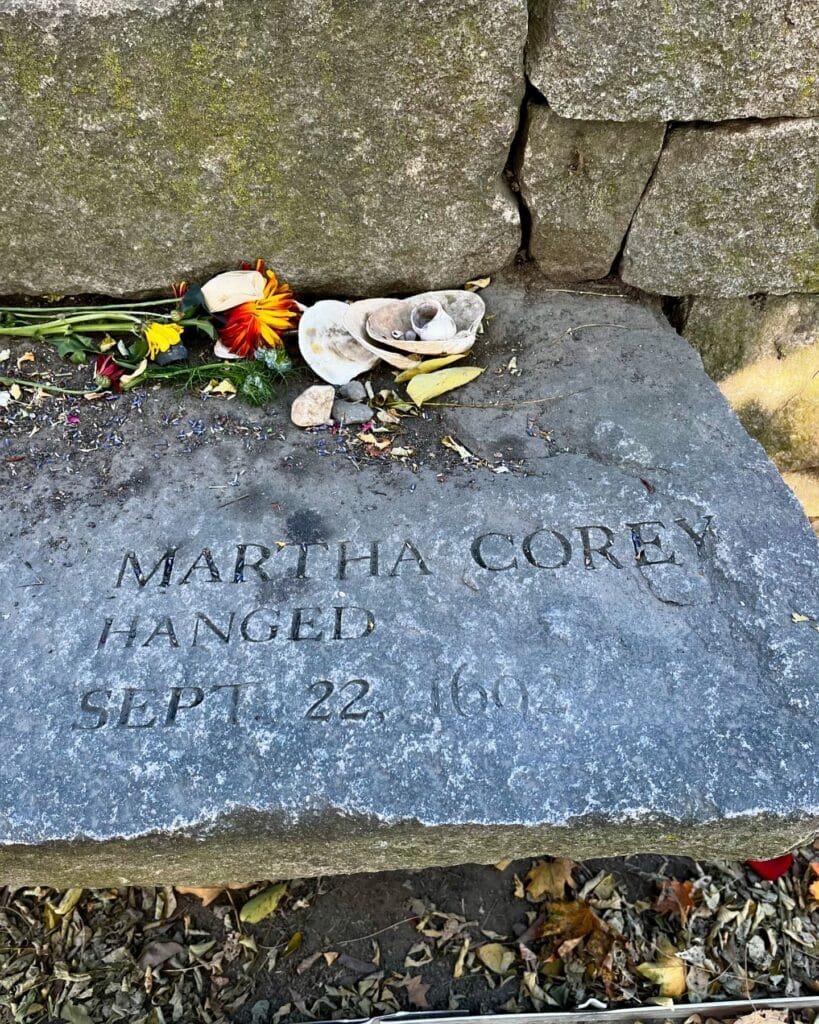  A memorial stone at the Salem Witch Trials Memorial in Salem, Massachusetts, honoring Martha Corey, engraved with her name and the date of her execution, September 22, 1692. Flowers and seashells rest on the stone as offerings.
