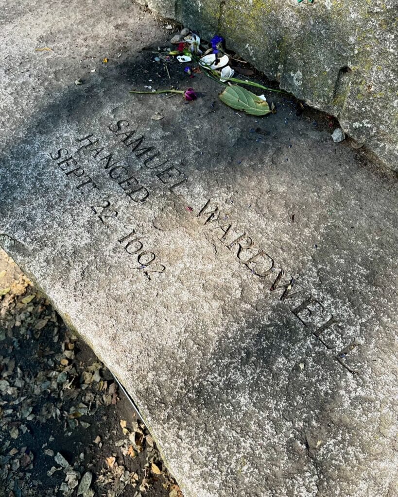  A memorial stone at the Salem Witch Trials Memorial in Salem, Massachusetts, honoring Samuel Wardwell, engraved with his name and the date of his execution, September 22, 1692. Flowers and seashells rest as tributes on the stone.