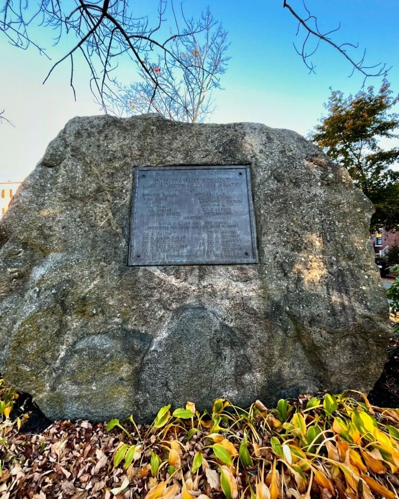 A large granite memorial stone with a plaque dedicated to the Twenty Third Regiment, surrounded by autumn leaves in Salem, Massachusetts.