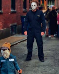 An adult and child dressed as Michael Myers from the Halloween movie series, wearing masks and dark blue coveralls, standing on a street in Salem, Massachusetts.