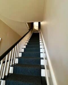 A narrow staircase inside the Salem Custom House in Salem, Massachusetts, featuring white railings, dark carpeted steps, and simple beige walls.