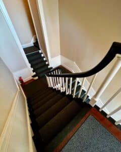 A view of narrow staircases inside the Salem Custom House in Salem, Massachusetts, featuring white railings, dark carpeting, and simple neutral walls with a classic design.