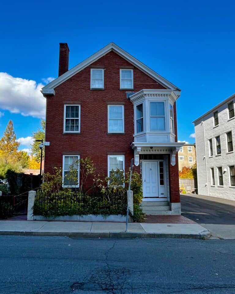The Nathaniel H. Felt House in Salem, Massachusetts, a historic red brick building with a white bay window and front door, surrounded by a small garden and iron fence.