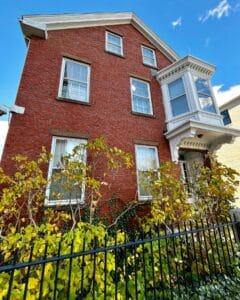 The Nathaniel H. Felt House in Salem, Massachusetts, a red brick building with a white bay window, black iron fence, and autumn plants in front.