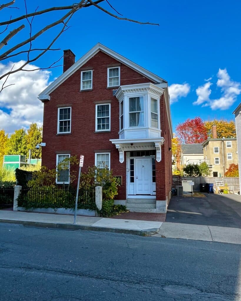 The Nathaniel H. Felt House in Salem, Massachusetts, a historic red brick building with a white bay window, granite steps, and a small garden enclosed by an iron fence.