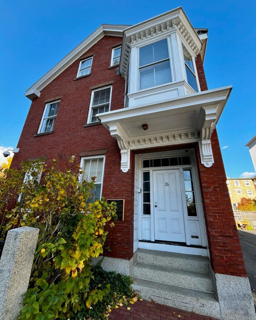 The Nathaniel H. Felt House in Salem, Massachusetts, a historic red brick building with a white bay window, granite steps, and a front entrance framed by autumn plants.