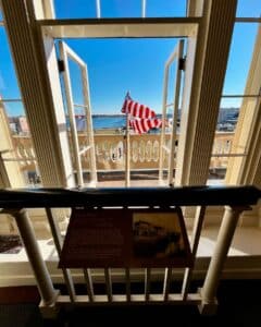 A view from the Salem Custom House in Salem, Massachusetts, showing an open balcony with the American flag, Derby Wharf, and Salem Harbor under a clear blue sky.