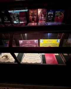 A display case at the Salem Witch Board Museum showcases Ouija-themed movies like "Ouijageist" and "Ouija Exorcism" alongside vintage Ouija boards and promotional materials.