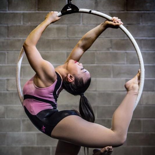 An aerial performer in Salem Massachusetts arching gracefully inside a suspended hoop, showcasing impressive flexibility at the Frozen Fire Festival.