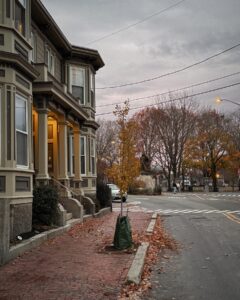 A peaceful street in Salem, Massachusetts during fall, showing the Roger Conant statue and a historic house with a tree-lined sidewalk.