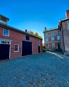 Rear courtyard of the Andrew-Safford House in Salem Massachusetts, featuring red brick buildings with black doors and windows under a clear blue sky.