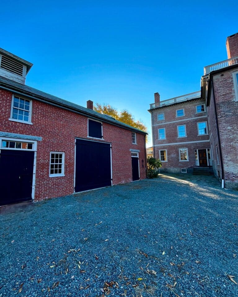 Rear courtyard of the Andrew-Safford House in Salem Massachusetts, featuring red brick buildings with black doors and windows under a clear blue sky.