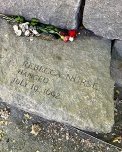 Memorial stone dedicated to Rebecca Nurse at the Salem Witch Trials Memorial in Salem Massachusetts, engraved with her name, the date July 19, 1692, and surrounded by roses and seashell offerings.