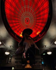 A vibrant red dome ceiling with a decorative grid pattern, and a hanging witch figure in silhouette, set against a dark and gothic interior at Blackcraft.