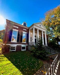 The Salem Athenaeum in Salem, Massachusetts, a historic brick building with tall white columns, black shutters, and a black iron fence on a sunny autumn day.