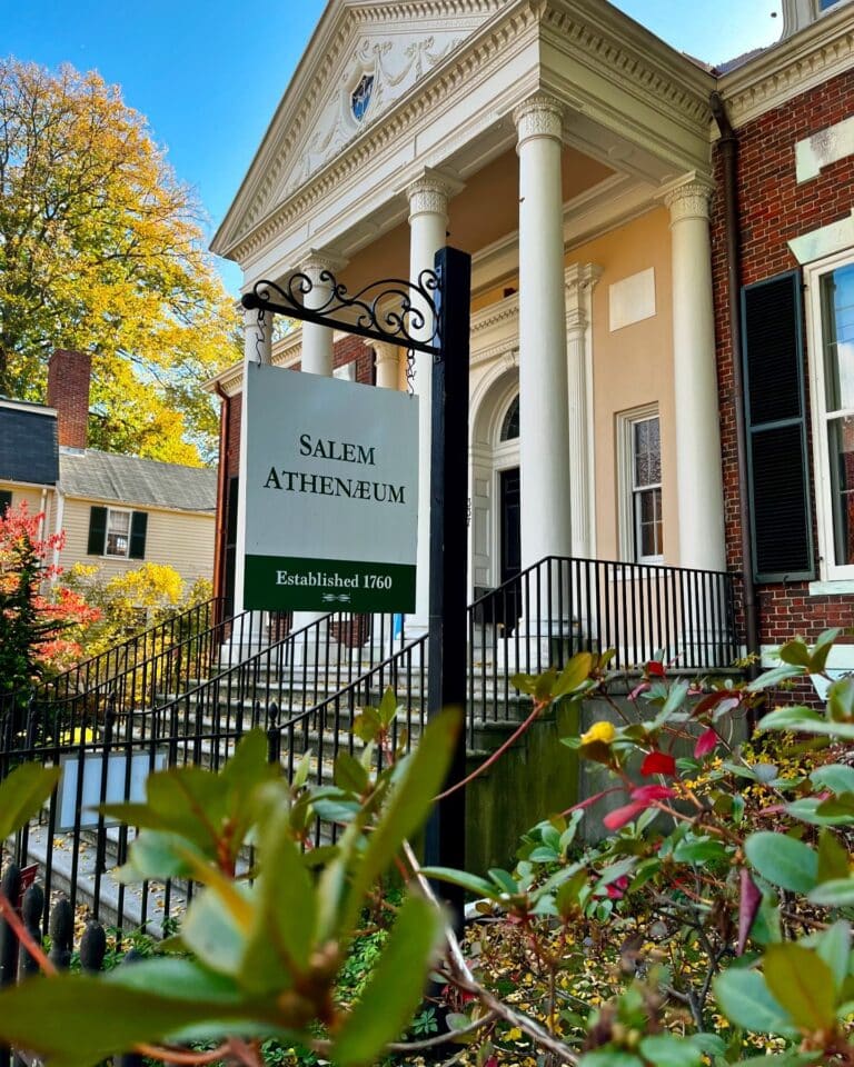 The Salem Athenaeum in Salem, Massachusetts, a historic brick library with white columns and a sign marking its establishment in 1760.