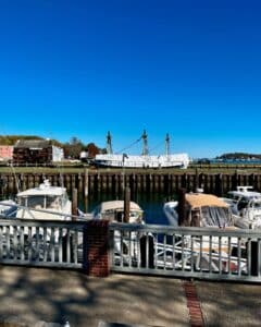 Boats docked at Salem Harbor in Salem, Massachusetts, with the historic tall ship, the Friendship of Salem, and the Custom House visible under a bright blue sky.