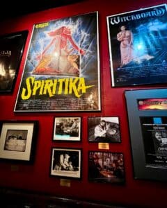 A vibrant display of movie posters, including "Spiritika" and "Witchboard," alongside black-and-white photographs depicting iconic scenes of people using Ouija boards.