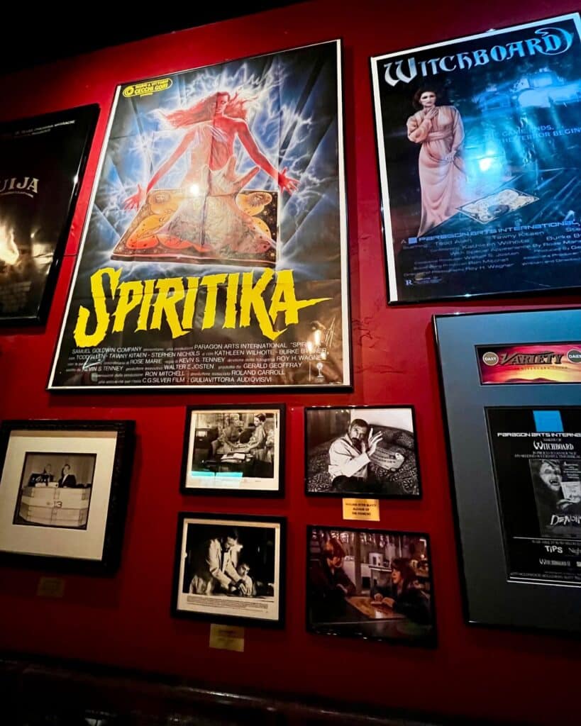  A vibrant display of movie posters, including "Spiritika" and "Witchboard," alongside black-and-white photographs depicting iconic scenes of people using Ouija boards.