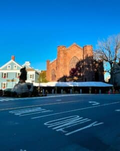The Salem Witch Museum in Salem, Massachusetts, featuring its Gothic architecture, flanked by neighboring historic buildings and a statue in the foreground, under a bright blue sky.