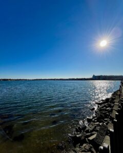 A serene view of the waterfront near the House of the Seven Gables in Salem, Massachusetts, featuring calm waters reflecting the sunlight under a clear blue sky.