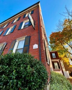 Angled side view of The Salem Inn's West House in Salem, Massachusetts, showcasing its red brick exterior, historical plaque, and vibrant greenery.