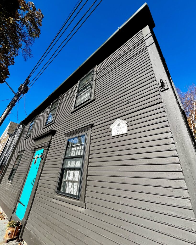 The Penn Townsend House in Salem Massachusetts, showcasing its gray wooden exterior with a bright blue door and a 1771 plaque.