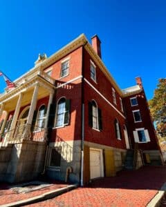 Side view of the Salem Custom House in Salem, Massachusetts, featuring red brick walls, green shutters, and the golden eagle against a clear blue sky.