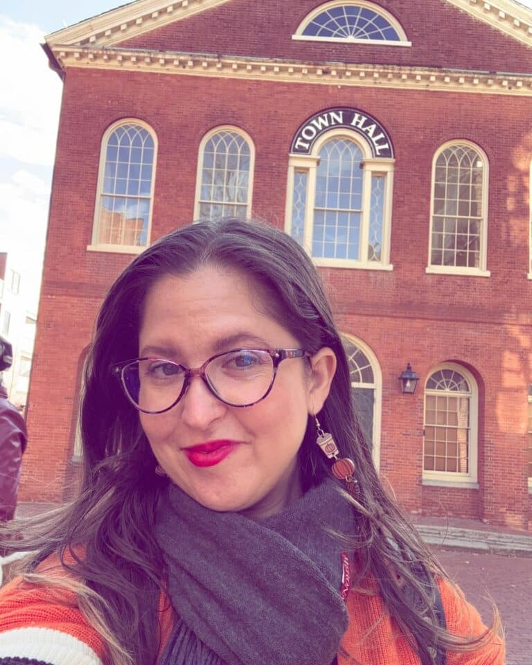 A person takes a selfie in front of the Old Town Hall in Salem, Massachusetts, with the historic red brick building and arched windows in the background.