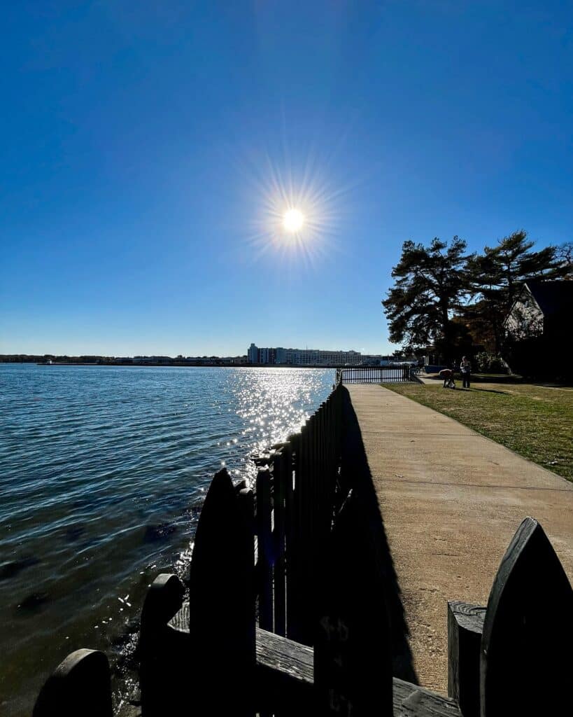 A bright sun over the waterfront near the House of the Seven Gables in Salem, Massachusetts, with a glimmering reflection on the water and a peaceful path.