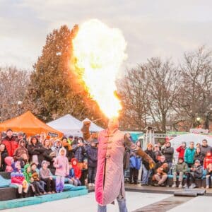 A fire breather in Salem Massachusetts creating a massive flame, captivating a bundled-up audience at the Frozen Fire Festival.