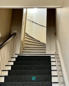 A narrow spiral staircase inside the Salem Custom House in Salem, Massachusetts, featuring dark carpeted steps, white walls, and a rope handrail leading to the upper floors.