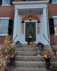 Halloween decorations on the steps of an old brick house in Salem Massachusetts, with pumpkins, witch hats, and fall plants.