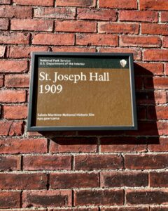The St. Joseph Hall sign from 1909 mounted on a historic brick wall at the Salem Maritime National Historic Site, featuring the National Park Service emblem.
