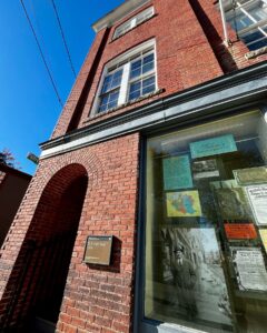 A striking red-brick building, St. Joseph Hall, dating to 1909, featuring an arched entryway and a display window showcasing historical information about Salem's immigrant history.