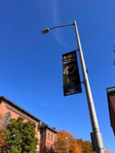 A tall streetlight with a banner reading 'Salem Haunted Happenings Since 1982' against a clear blue sky, with colorful autumn trees and red brick buildings in the background in Salem, Massachusetts.