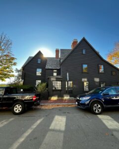 The historic House of the Seven Gables in Salem, Massachusetts, bathed in sunlight with two parked vehicles in the foreground.