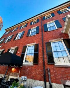 Upward view of the Salem Inn West House in Salem Massachusetts, featuring its red brick facade, black shutters, and classic colonial windows.