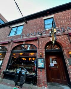 The exterior of Turner's Seafood restaurant located in the historic Lyceum Hall in Salem, Massachusetts, showcasing a brick facade, arched windows, and the restaurant's sign above the entrance.
