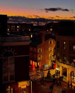 Downtown Salem with buildings illuminated against the backdrop of a vibrant sunset, showcasing colorful orange and blue hues in the sky while the street lights below bring the city to life.